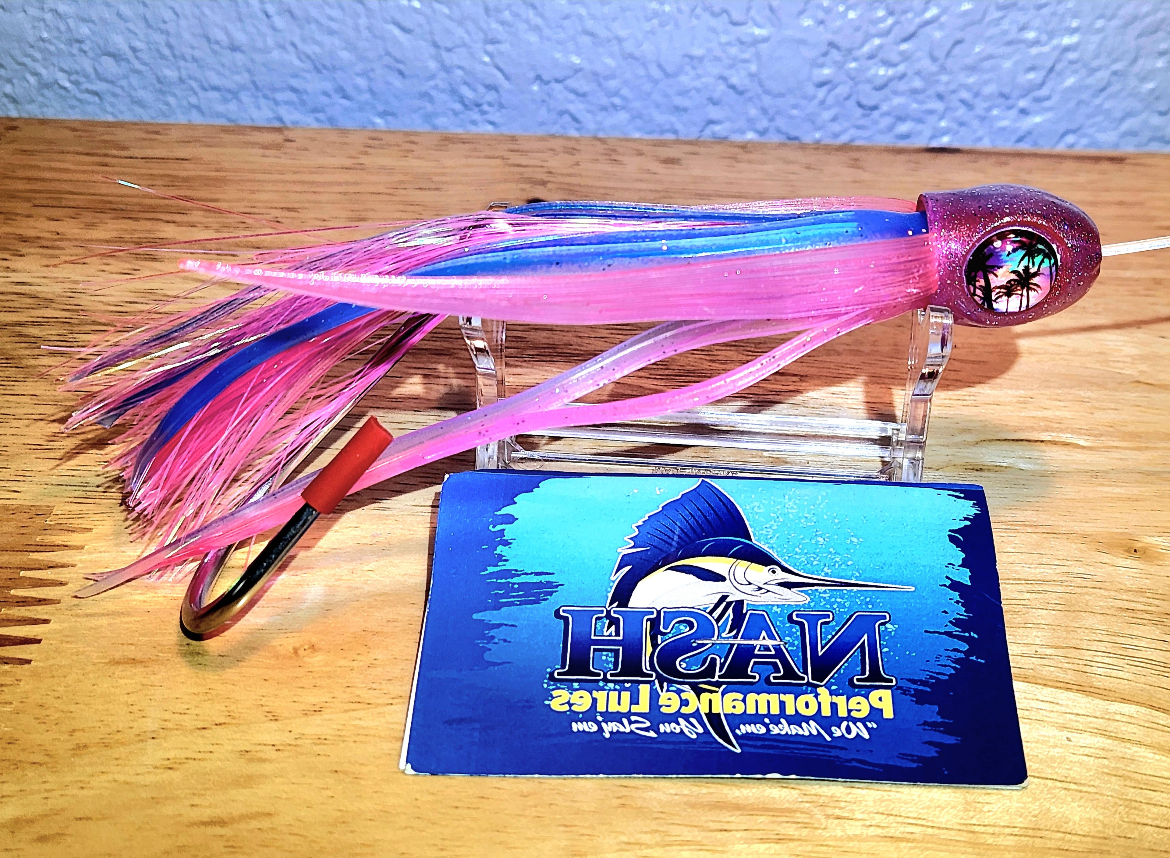Fishing lure with pink and blue details on a wooden surface, branded 'Nash Performance Lures'.