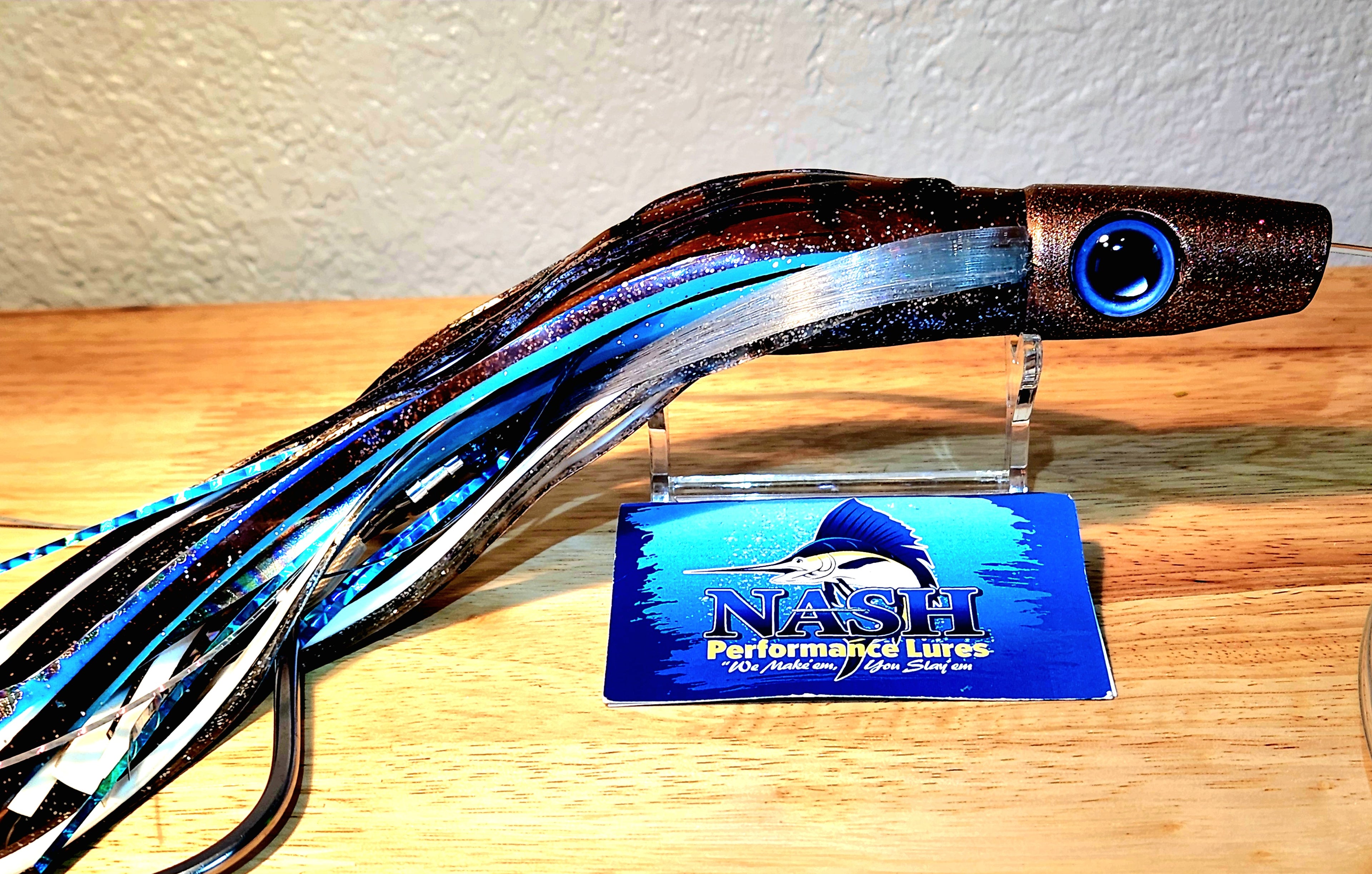 Fishing lure with a blue and black pattern on a wooden surface, branded 'Nash'.